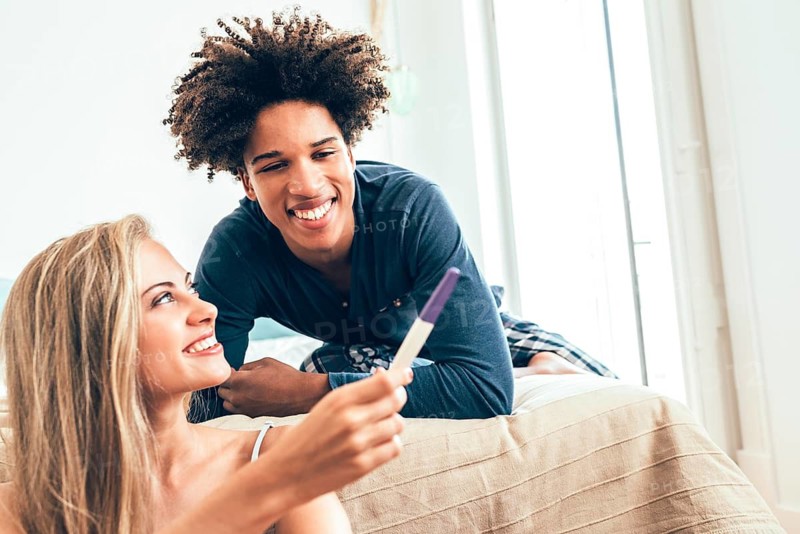 A happy couple smiling at a positive pregnancy test in a sunlit room. The image captures the excitement and love shared in this intimate moment of discovery