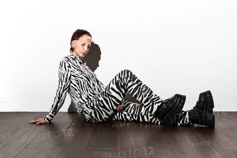 Fashion model in a striking animal print outfit poses against a white backdrop, highlighting the dramatic contrast of patterns. Captured with flash photography in a studio setting