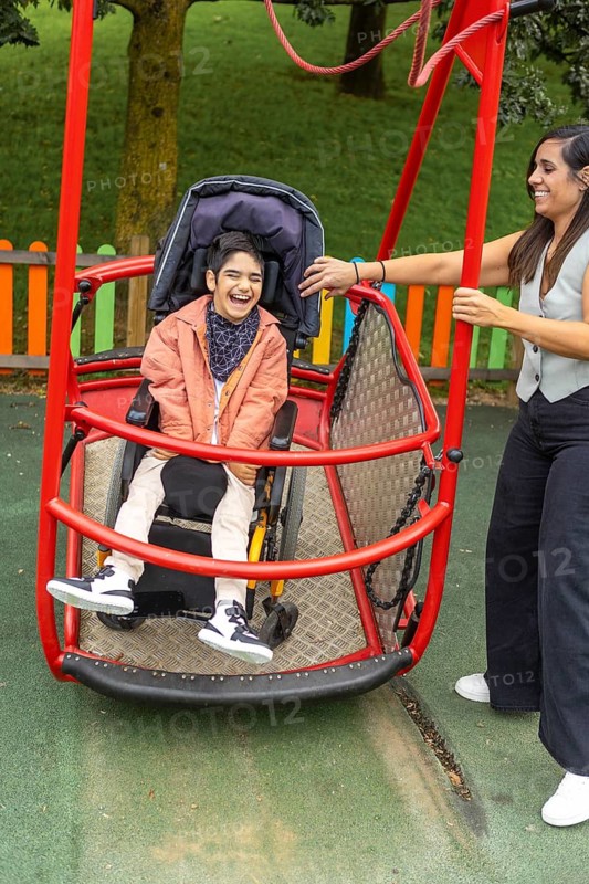 A child with cerebral palsy in a wheelchair enjoys an inclusive playground swing, assisted by a mother. Vibrant outdoor setting promotes accessibility and joy for all children