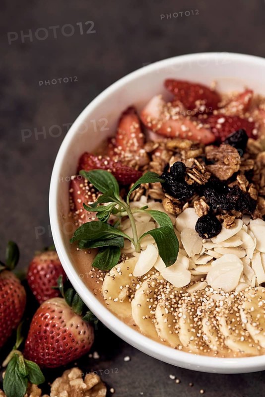 A breakfast natural bowl featuring fresh strawberries, bananas, nuts, and granola, sprinkled with quinoa. Perfect for a nutritious start, set on a rustic background