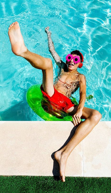 A teenage boy enjoys a sunny pool day, wearing red headphones and pink flower-shaped sunglasses. The vibrant scene captures the essence of summer fun and relaxation