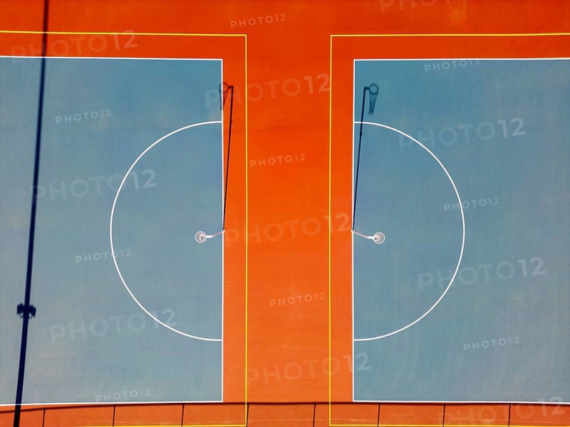 Top view capturing the vibrant, perfectly aligned netball courts in Canberra. The aerial perspective emphasizes the bold contrast between the colors of the playing surface marked with white lines, presenting an eye catching geometric pattern