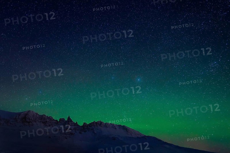 The stunning Northern Lights illuminate the starry sky above a snowy mountain range in Iceland, creating a mesmerizing winter scene. Perfect for nature and travel themes