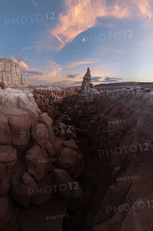 Stunning view of Goblin Valley State Park in Utah, showcasing unique sandstone formations under a colorful sunset sky and a crescent moon. A perfect blend of nature's artistry
