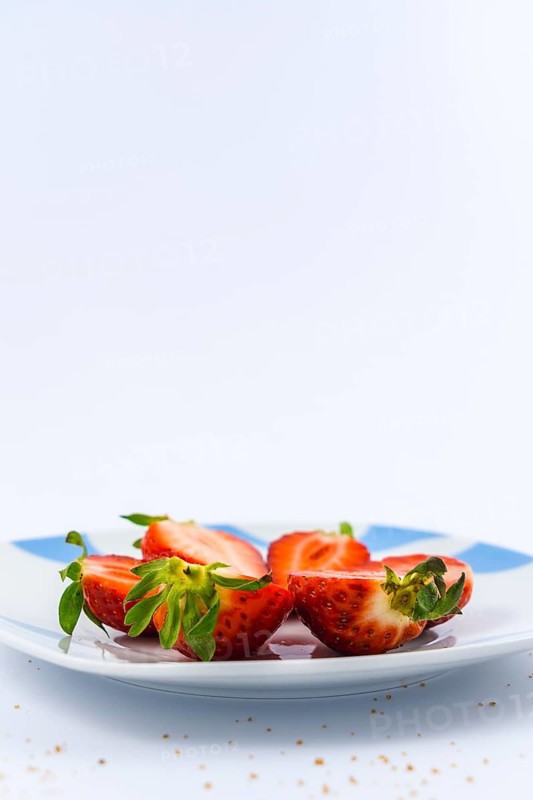 Strawberries cut into a white plate with a white background with brown sugar