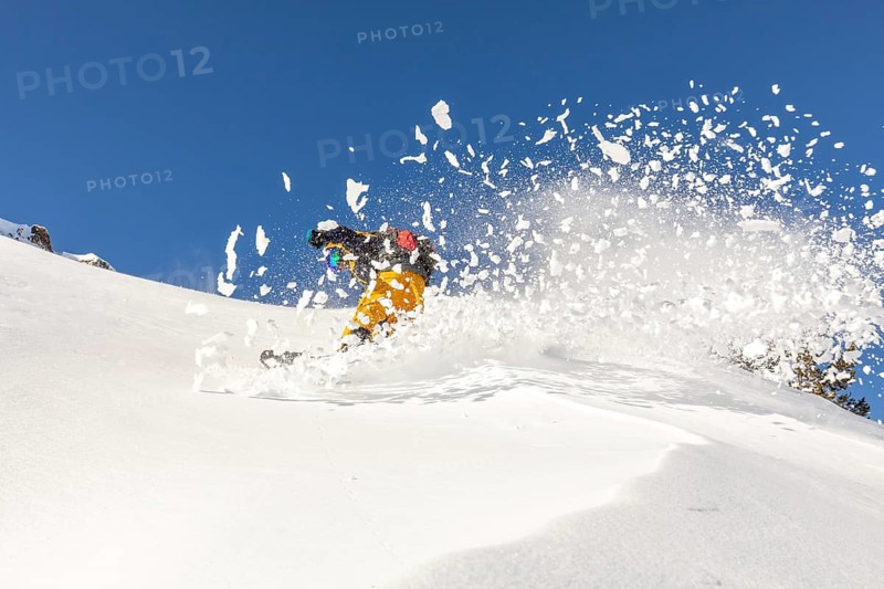 Snowboarder expertly carves through fresh powder on a sunny winter day, showcasing the thrill of freeride snowboarding in the backcountry
