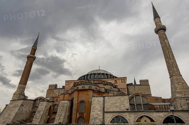 Dramatic view of Hagia Sophia, with dark clouds looming above its majestic minarets and domes. This iconic Istanbul landmark stands as a testament to centuries of history and architectural splendor