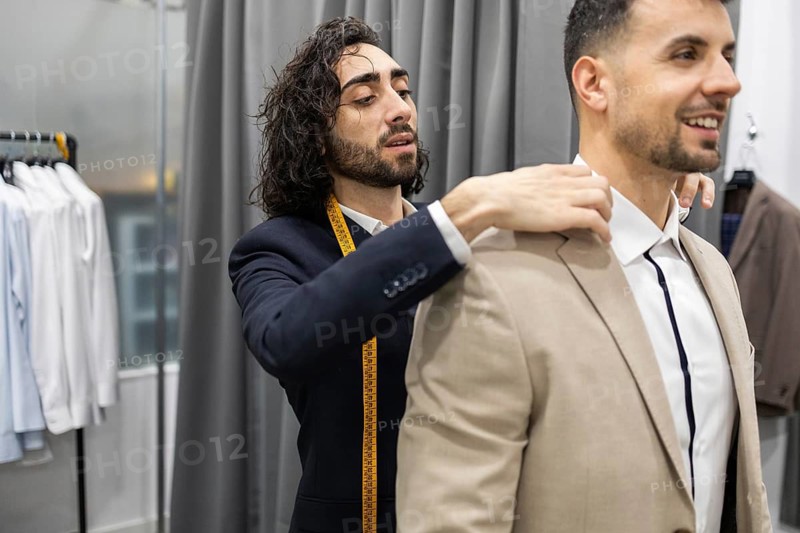 A tailor is attentively adjusting a client suit jacket in a suit store. The focus is on precision and creating the perfect fit for the customer