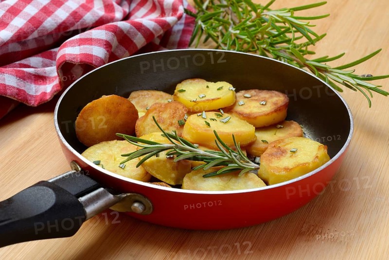 Fried potatoes in pan with rosemary sprig