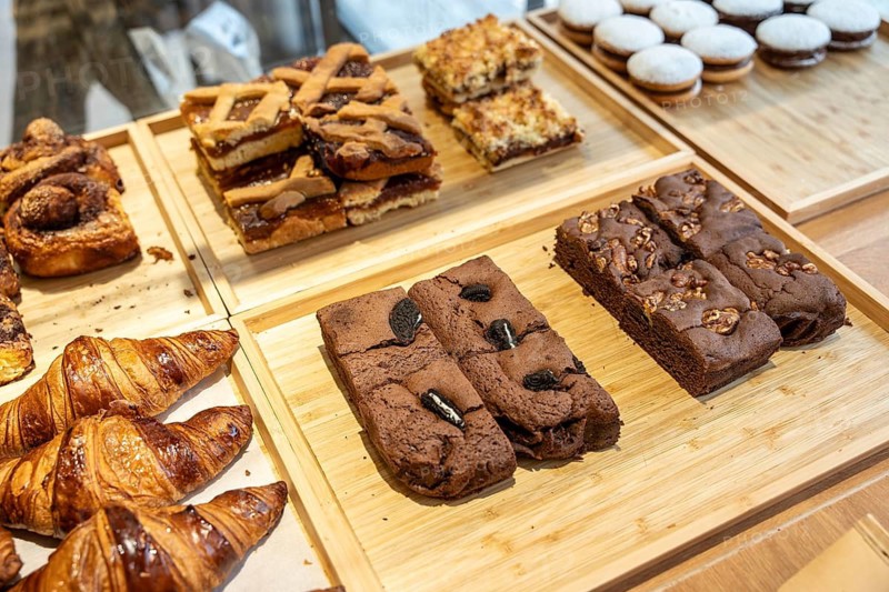 Various baked goods including croissants, tarts, and brownies arranged on wooden trays, showcasing a tempting selection of sweet treats in a bakery or shop