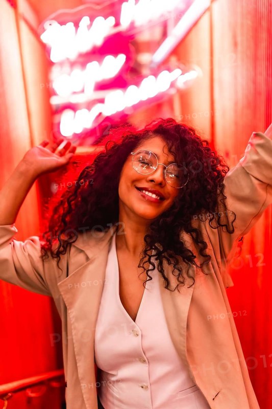 Vertical portrait of a happy beautiful latin woman with chic clothes and curly hair dancing next to red neon lights