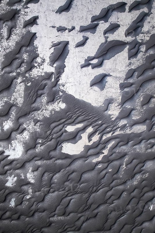 Close-up image capturing the intricate textures of black sand alongside peeling white paint, emphasizing natural and man-made contrasts