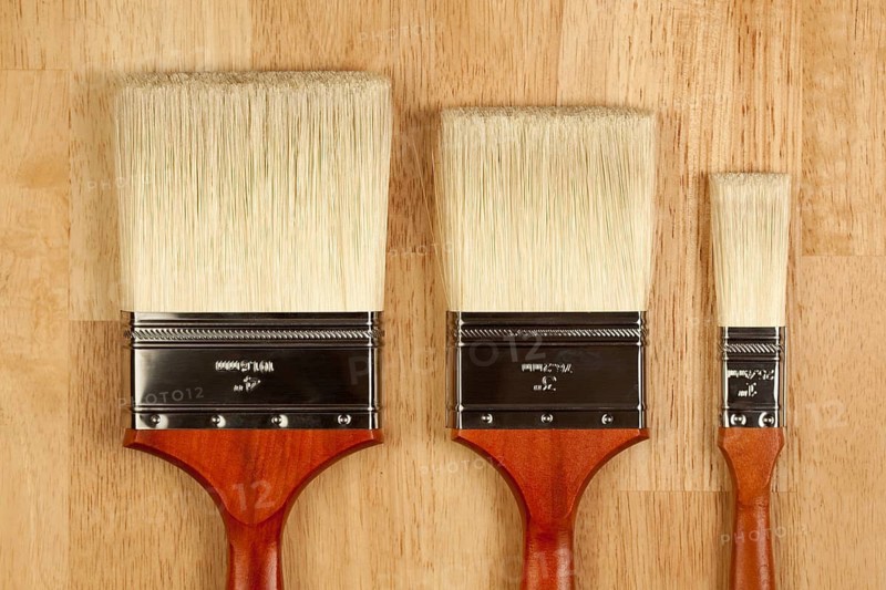 Three Different Sized New Paint Brushes on a Wood Surface