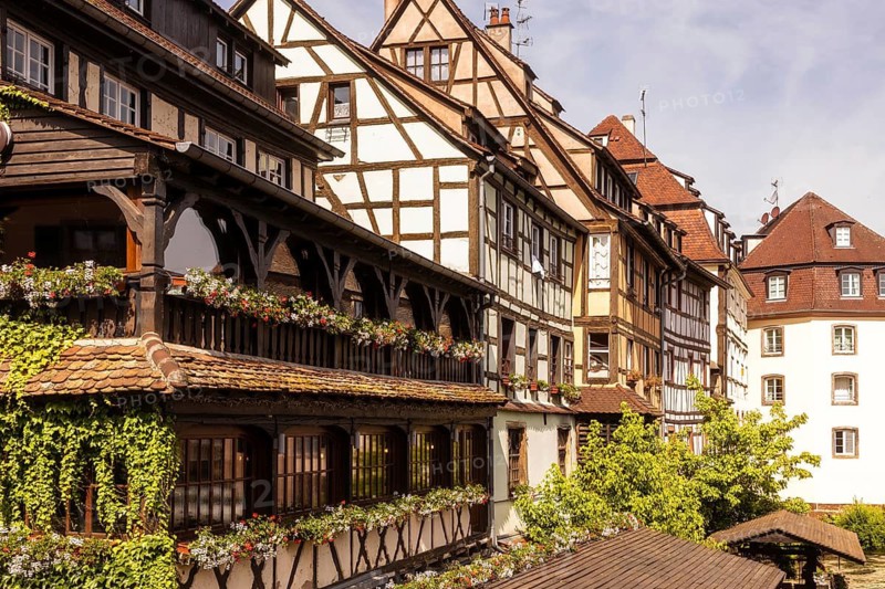 Picturesque view of traditional half timbered buildings adorned with flower boxes, showcasing the quaint architectural charm of Strasbourg, France, under a clear blue sky