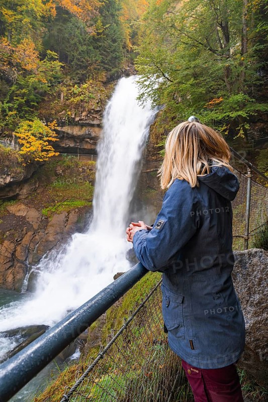 A woman stands at a railing and looks at a large waterfall in autumn forest, Lake Brienz, Giessbach Waterfall, Switzerland