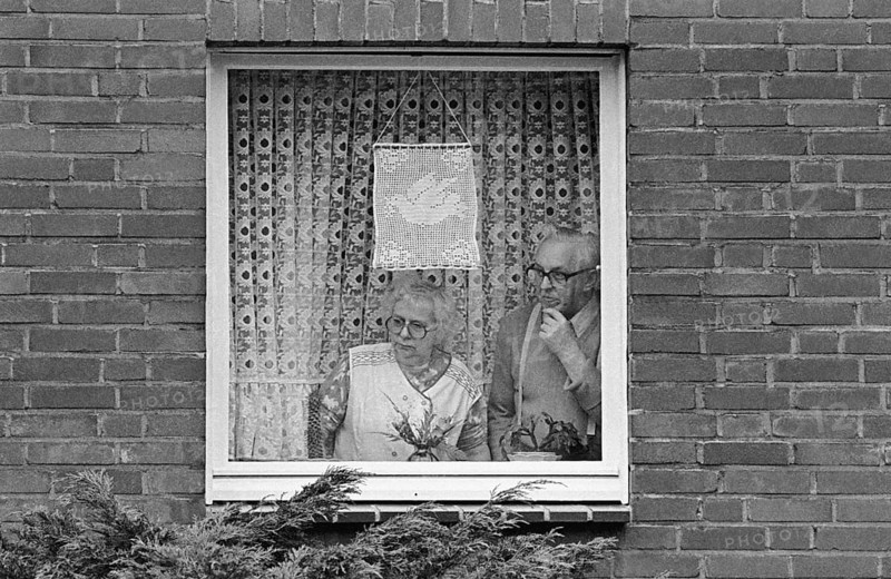 A retired couple looks out the window of their apartment at the passing Ruhr Easter March 1983. They show their sympathy for the peace march with the motif of a dove of peace, Essen, Germany