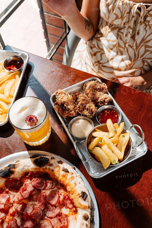 A flavorful spread featuring crispy fried chicken, potato dippers with assorted sauces, and wood-fired pepperoni pizza, accompanied by a refreshing cocktail in a casual dining setting