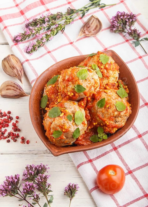 Pork meatballs with tomato sauce, oregano leaves, spices and herbs in clay bowl on a white wooden background with linen textile. side view, close up