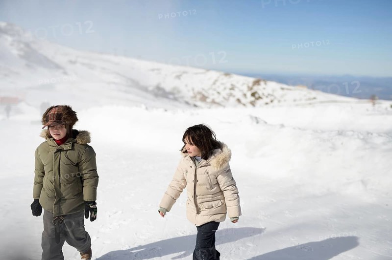 Two children in warm jackets walk through the snowy landscape at Sierra Nevada Ski Resort, Granada, showcasing a beautiful winter day and outdoor fun