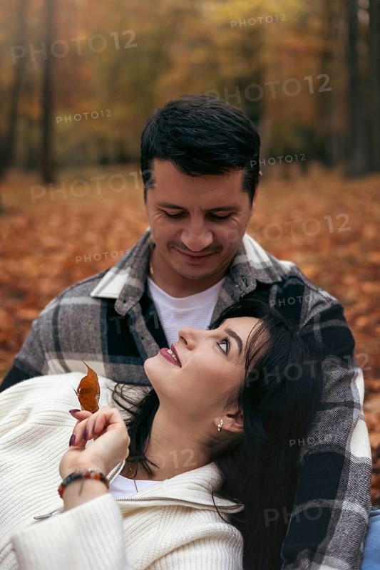 A couple shares a tender moment surrounded by the vibrant colors of autumn leaves in a wooded area. The warm atmosphere embodies love and togetherness in a natural setting