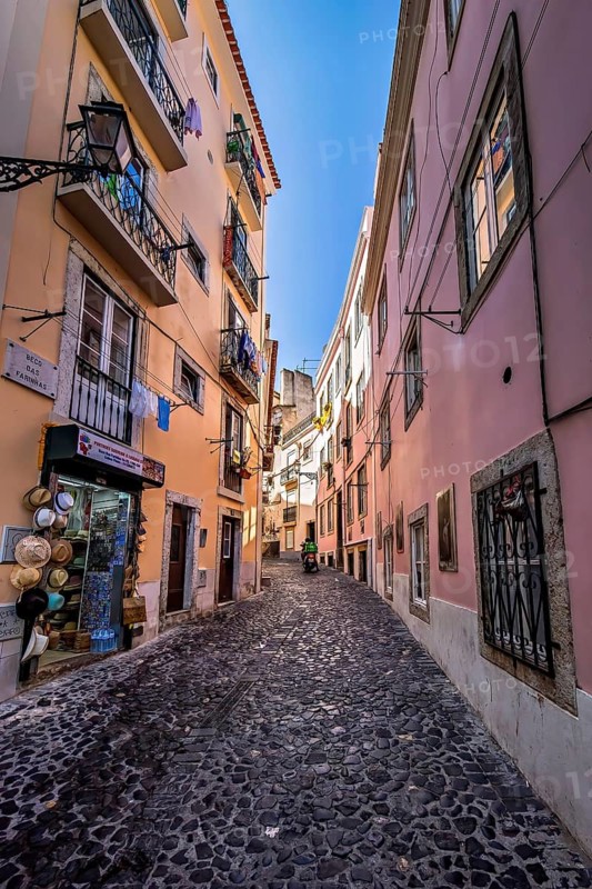 Cobblestoned narrow street lined with colorful buildings under a blue sky, Alfama, Lisbon