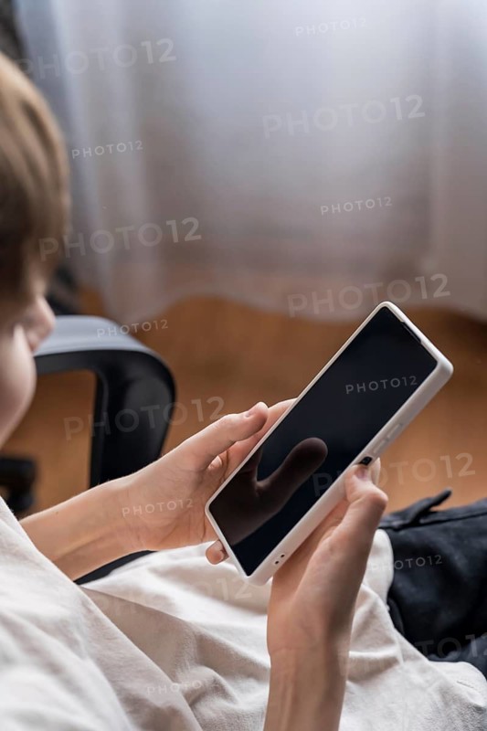 A teenager engrossed in his smartphone, presumably preparing to play. The scene captures youthful concentration and a modern, tech-savvy lifestyle in a casual setting