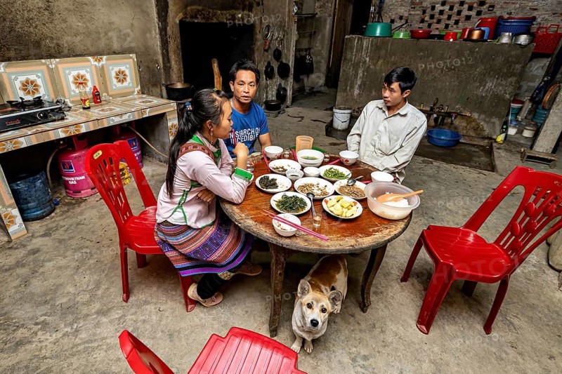 Family eating together in a rustic kitchen. A dog sits on the floor, a farmer's family having dinner together in the Sa Pa area of Vietnam