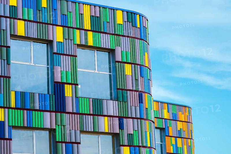 A vibrant, curved building facade featuring multicolored panels in shades of yellow, blue, and green under a clear blue sky