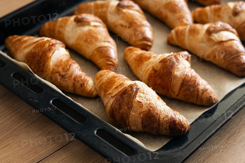 A batch of golden brown homemade croissants rests on a baking tray, showcasing their flaky, buttery layers. Perfectly baked, they offer an inviting aroma and irresistible taste