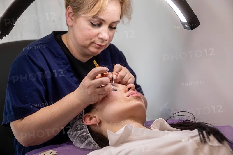 A beauty professional meticulously applies eyelash extensions in a salon setting. The scene captures skill and focus, highlighting the artistry of modern beauty treatments