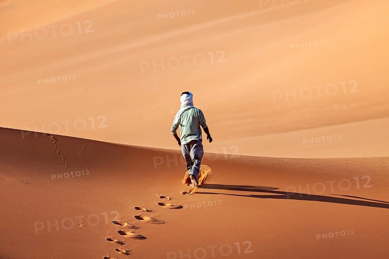 Person walks alone over sand dunes, leaves footprints in the golden desert sand, Tuareg walks through the endless dunes and sandy landscape of the Sahara in Algeria