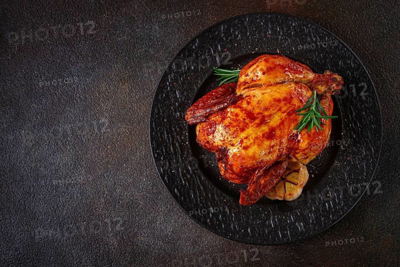 Baked chicken on a black dish with herbs and garlic, on a dark background, homemade, no people