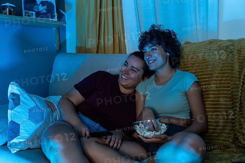 A joyful lesbian couple eating popcorn while watch tv, highlighting domestic harmony and love