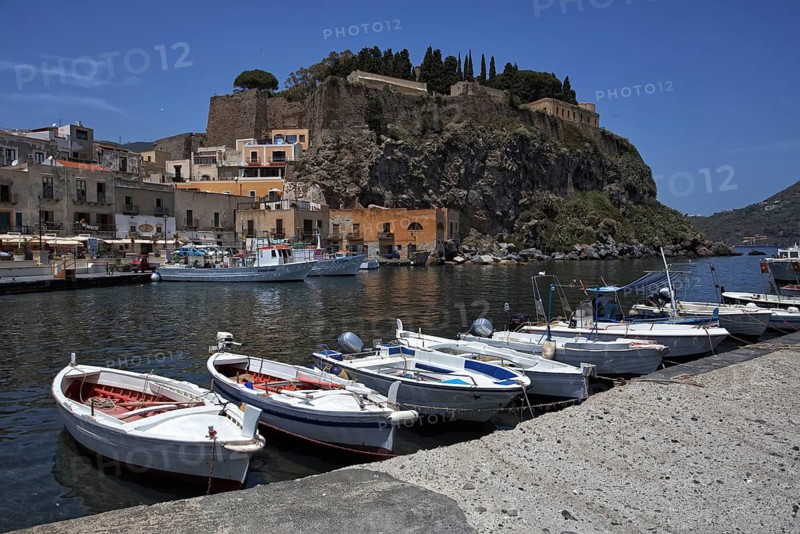 Boats are lying in the water of a harbor in front of a rocky mountain face and old buildings, Lipari City Lipari Islands Sicily Italy
