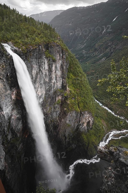 A breathtaking view of a mighty waterfall cascading down verdant cliffs in Norway's stunning mountain terrain, perfect for road trips, trekking, and camping adventures