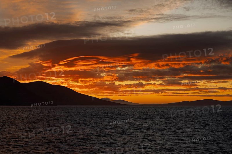 Sunset with orange cloud formations over silhouetted hills and sea, Falkland Islands