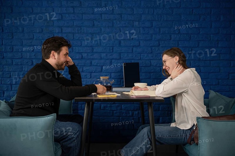 Two friends enjoying a casual conversation in a cozy cafe setting. They are seated at a table with books, notes, and tea, creating a relaxed and friendly atmosphere