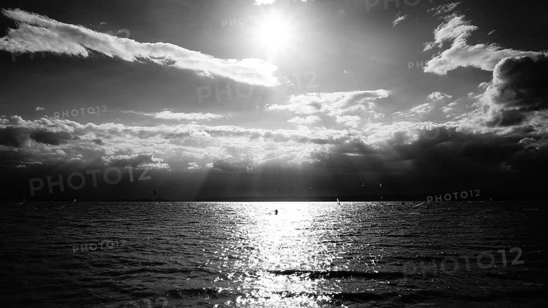 Monochrome, sunlight breaks dramatically through clouds and is reflected on Lake Neusiedl, Austria