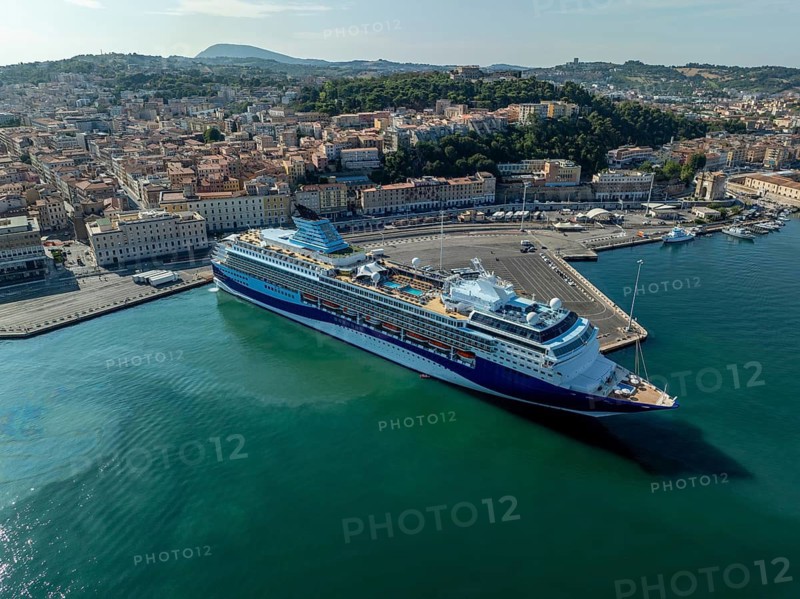 Aerial view of a large ocean liner docked at the bustling port, Italy, with the city's historic architecture and lush hills providing a stunning backdrop