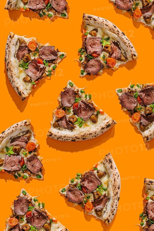 Top view of delicious pizza slices, tastefully topped with roast beef, truffle sauce, mozzarella, porcini mushrooms, and fresh cherry tomatoes. Each slice is generously garnished with green onions on a vivid orange background