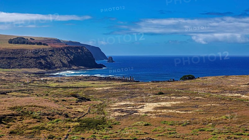 Wide view of green landscape with distant moai and blue coast, the Moai statues on Easter Island in the Pacific Ocean