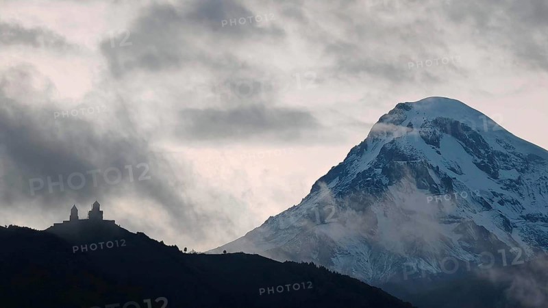 Silhouette of a Gergeti church in front of a spectacular snow-capped mountain Kazbek, Kazbegi in twilight, Stepantsminda, Georgia