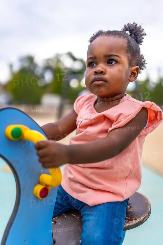 Vertical close-up of a cute african girl sitting on colorful swing in the playground