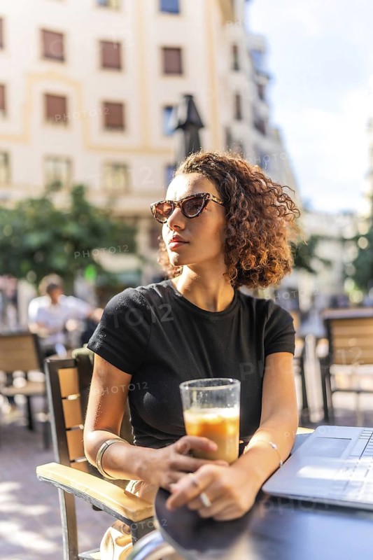 Vertical photo of a beauty arab woman drinking coffee in an outdoor cafeteria in a sunny day of summer in the city