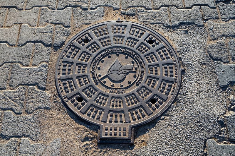 A detailed manhole cover with exemplary structures on an asphalted road, Fethiye, Mugla, Aegean Sea, Turkey