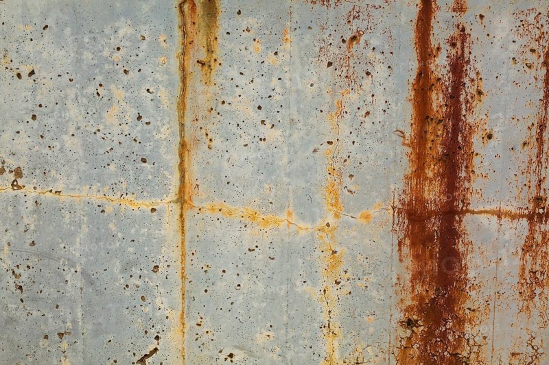Close-up of long brownish rust streaks, yellow orange stains and small holes on old light greyish blue painted concrete wall surface in poor and damaged condition, Quebec, Canada