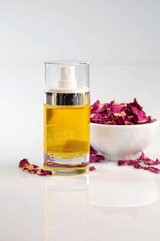A beautiful glass bottle filled with aromatic essential rose oil stands elegantly beside a bowl of vibrant dried rose petals, creating a peaceful and inviting atmosphere