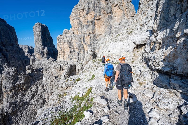 Three mountaineers on an exposed rock band, Via Ferrata Bocciere Centrale via ferrata, spectacular mountain landscape with steep rock faces and rock towers, Brenta Mountains, Parco Naturale Brenta-Adamello, Trentino, Italy