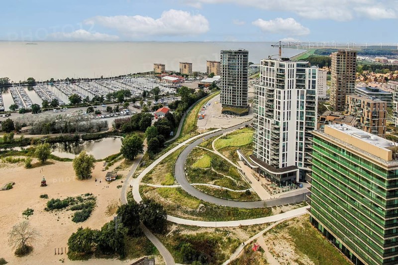 A scenic view showcasing modern buildings alongside a marina. The natural landscape merges with urban architecture, highlighting the harmony of city and nature