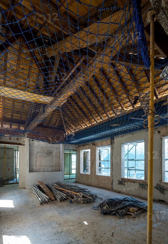 Interior view of an abandoned building under renovation. Scaffolding and construction materials are scattered on the floor, with sunlight streaming through the windows